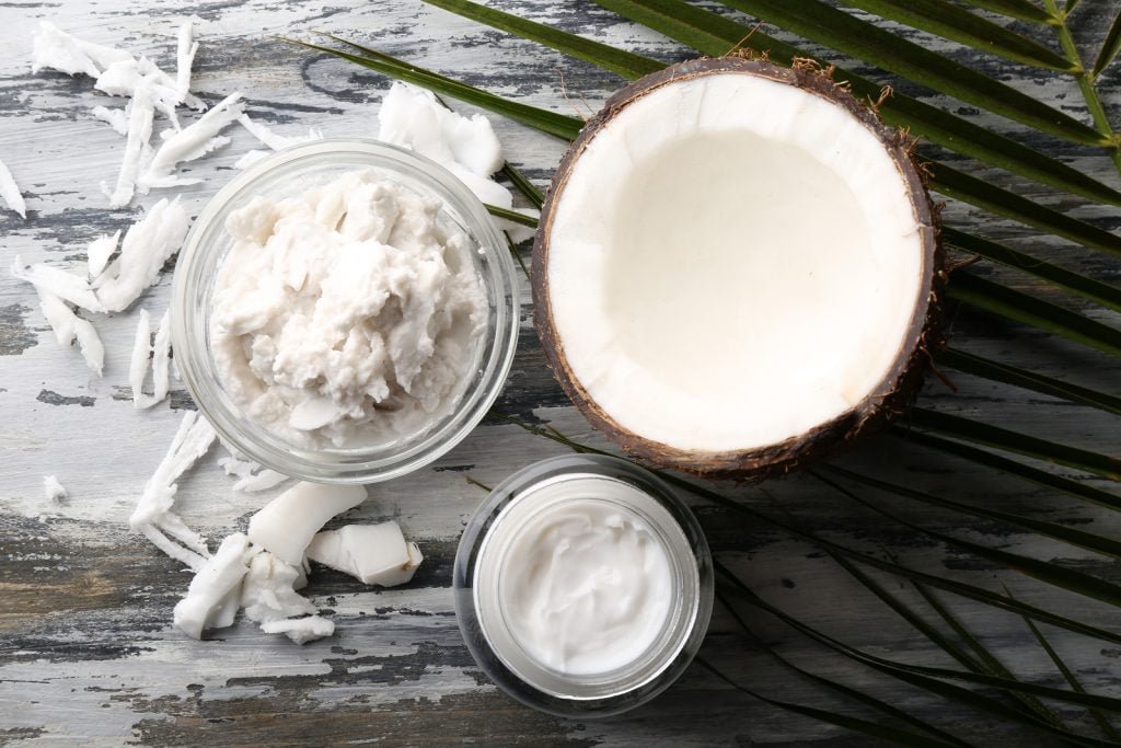 Coconut with coconut oil in bowl with jar of cosmet